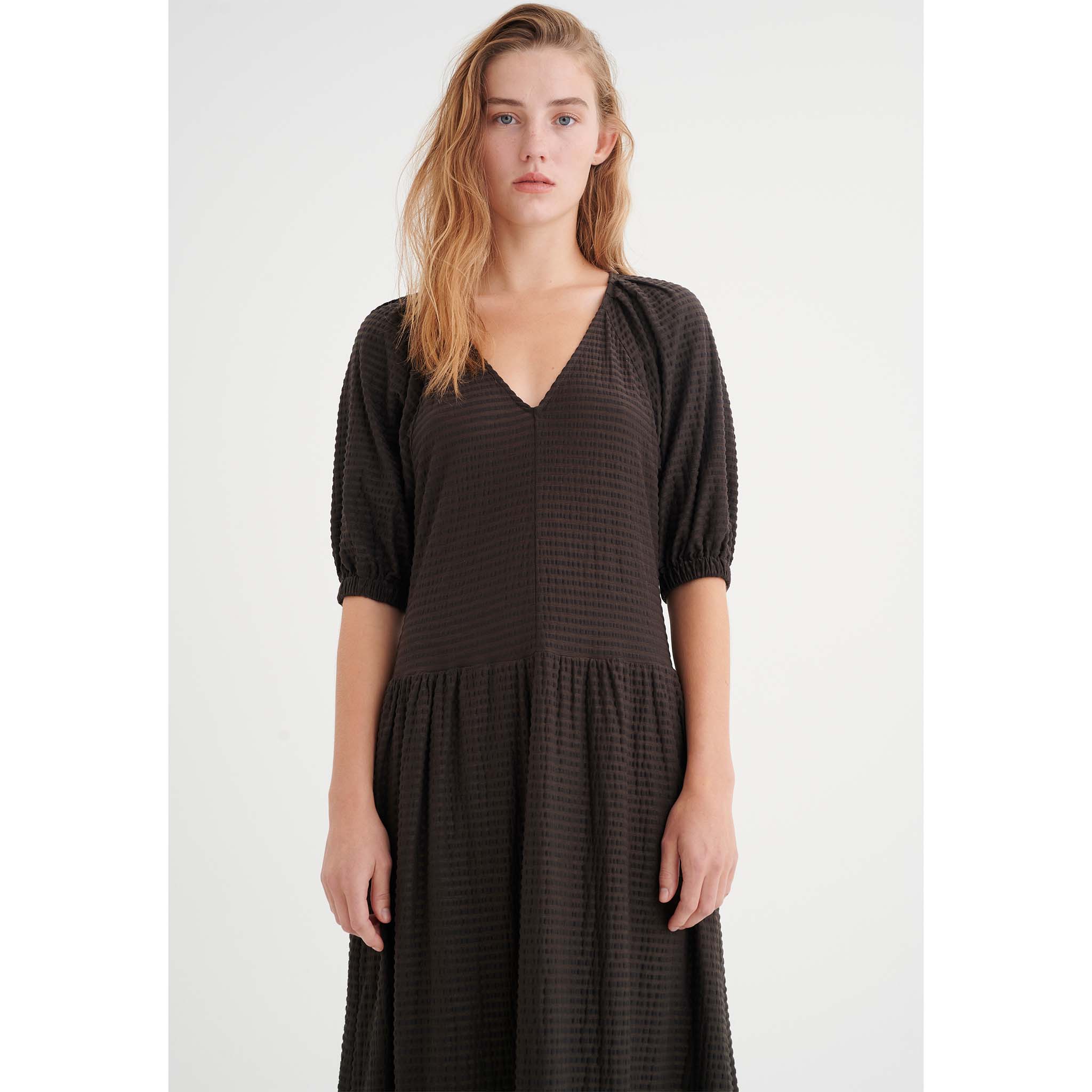 In Wear, tummanruskea, pitkä mekko. Väljät hihat, poimutettu helma. Lähikuva mallin päällä.