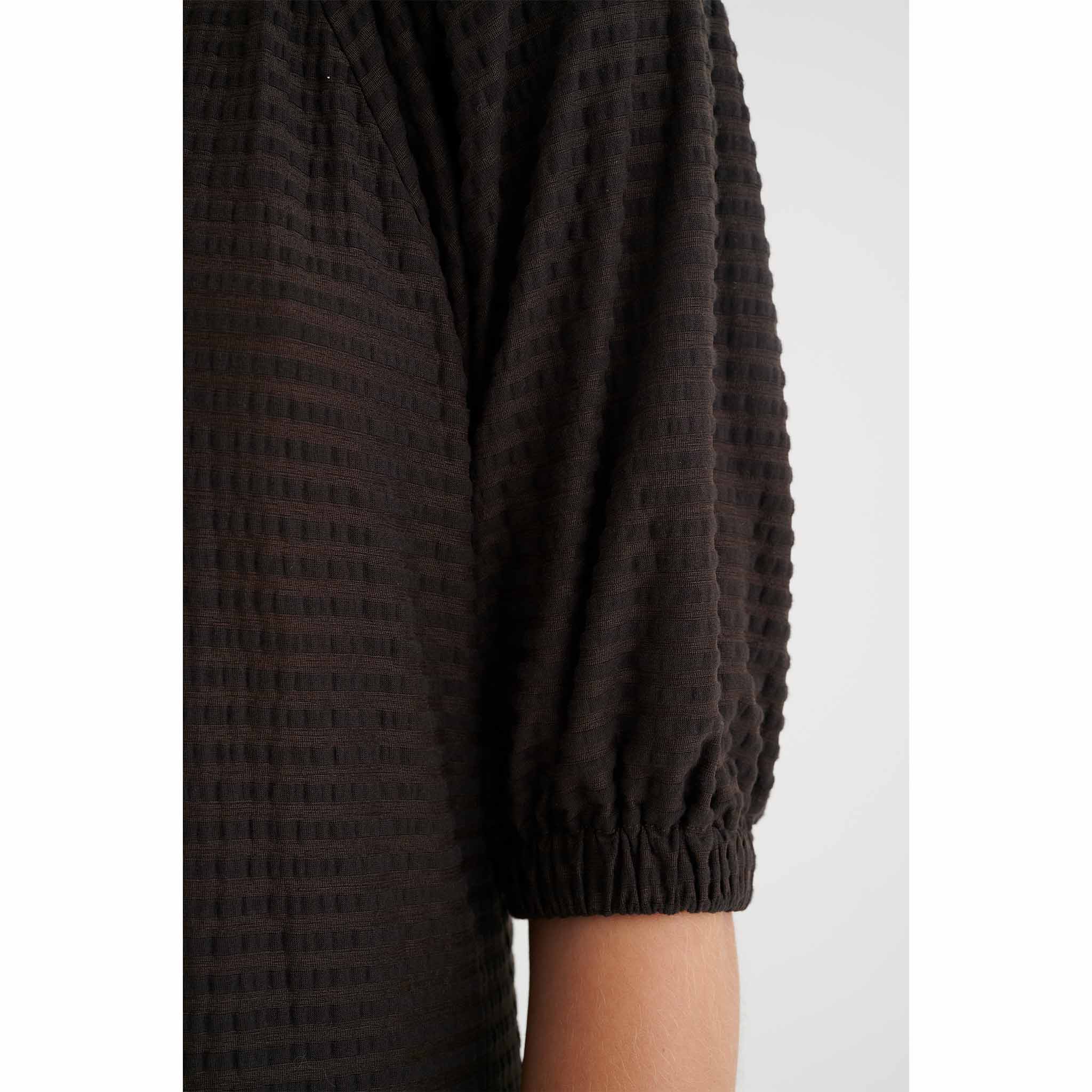 In Wear, tummanruskea, pitkä mekko. Väljät hihat. Lähikuva mallin päällä.